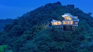 Une maison moderne dotée d’un grand balcon, entourée d’une forêt dense.