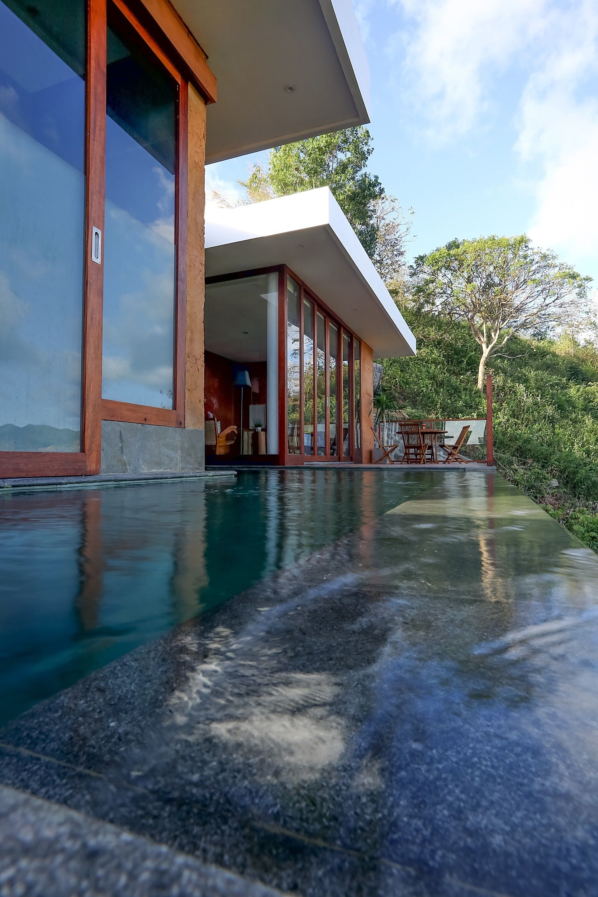 A modern house with a swimming pool, large windows, and a patio with outdoor furniture.