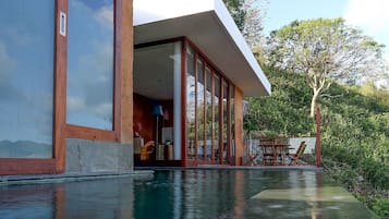 A modern house with a swimming pool, large windows, and a patio with outdoor furniture.