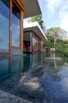 Una casa moderna con piscina, ventanas amplias y un patio con mobiliario exterior.