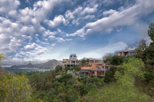Una zona residencial costera con casas modernas, abundante vegetación y vistas al mar y las montañas.