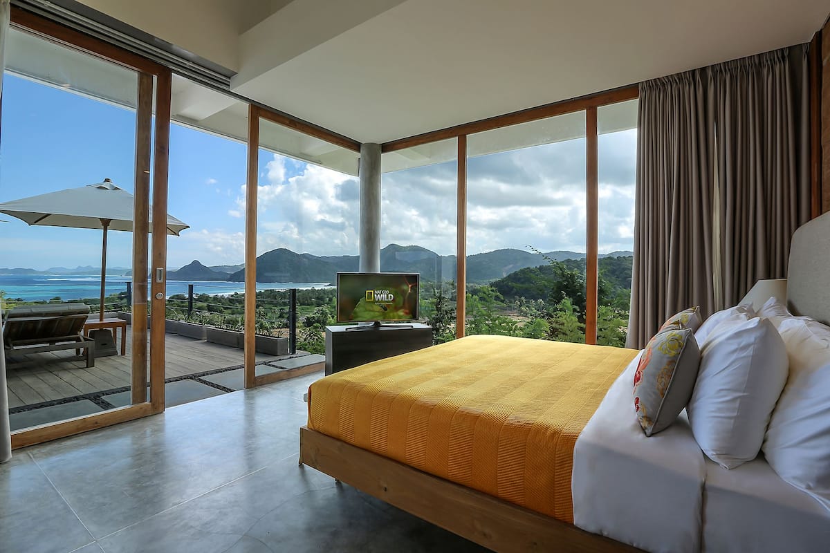 A bedroom with a large bed, a TV, and a view of the ocean.