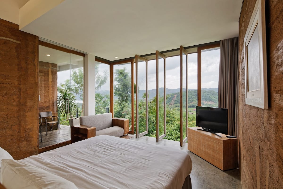 A modern hotel room with a large bed, a TV, and a seating area with a view of the outdoors.