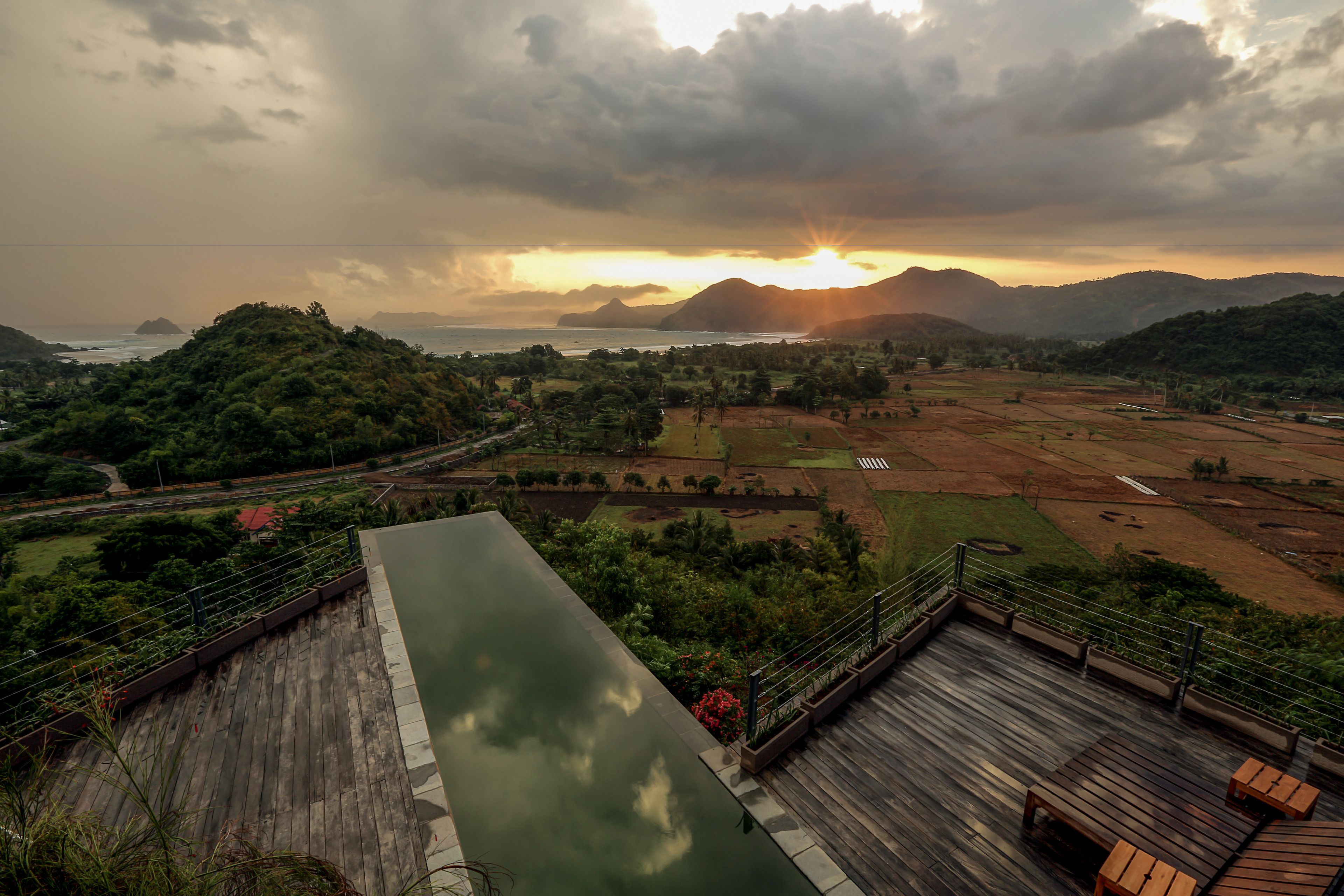A rooftop terrace with a view of the sunset over mountains and the sea.