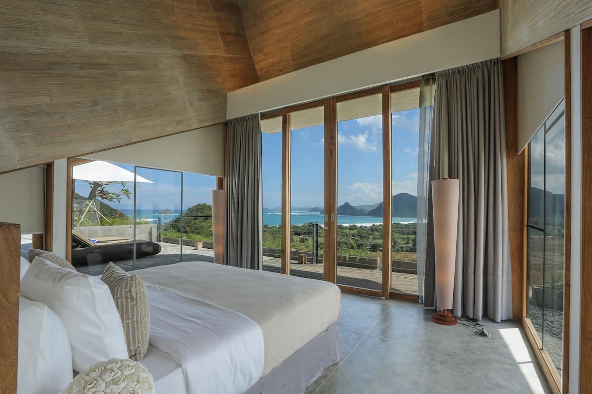 A spacious bedroom with a large bed, a view of the ocean, and a balcony.