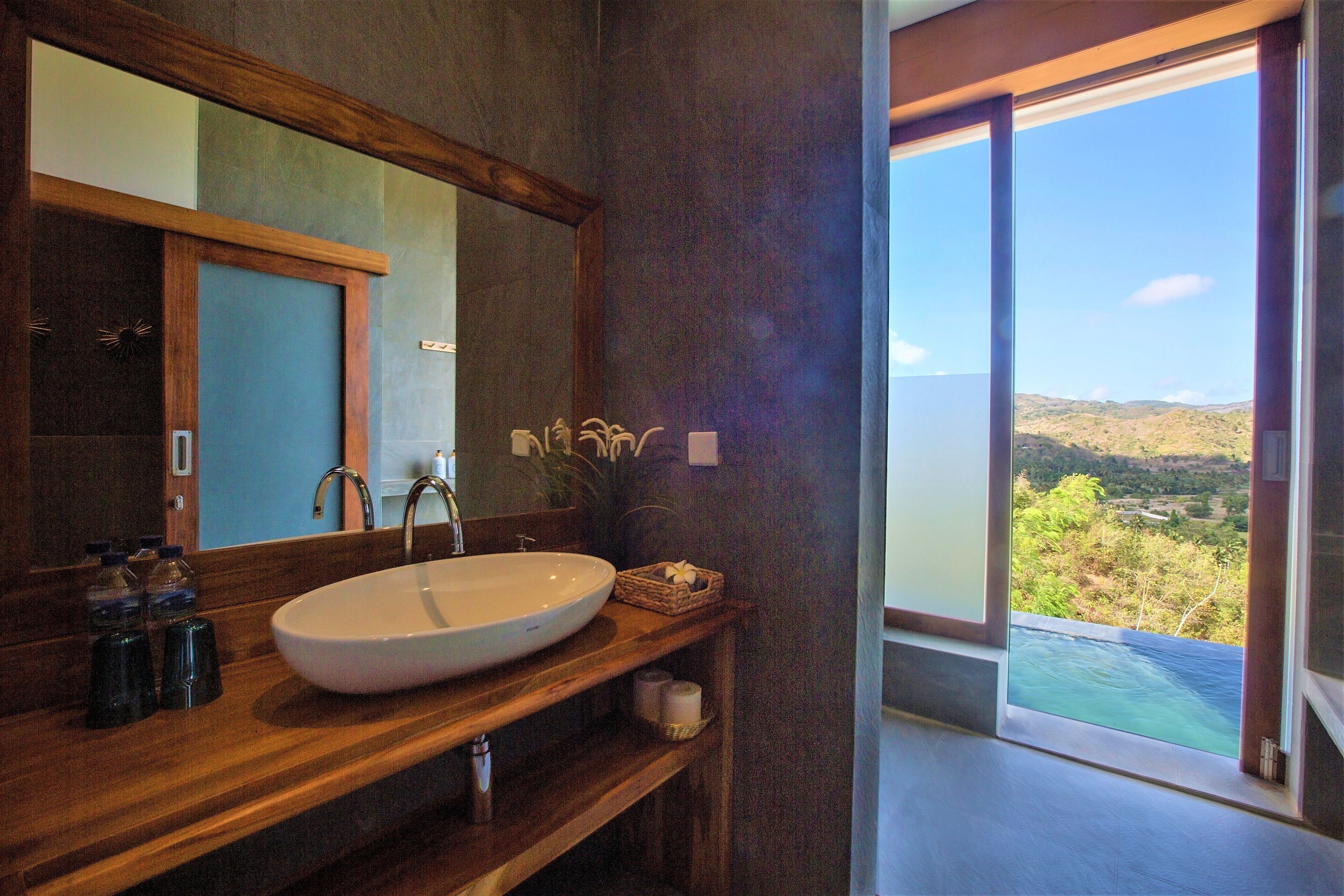 A bathroom with a large mirror, wooden vanity, and a view of a landscape through a glass door.