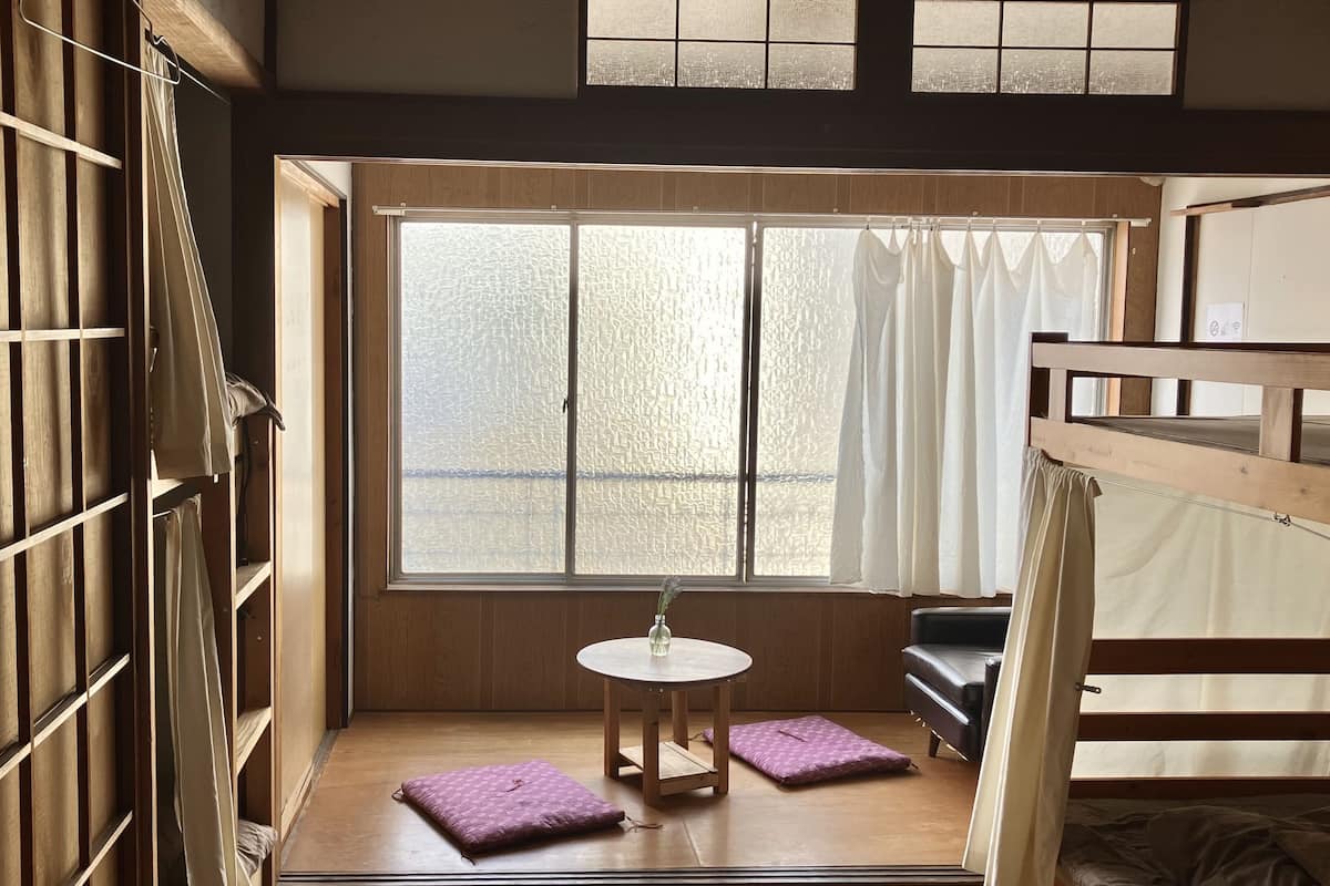 A room with a bunk bed, a small table with a vase, and a window with curtains.