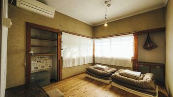 A room with a wooden floor, a bed with a white blanket, a small table, a shelf with a plant, and a sign about an emergency ladder.