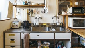 Une cuisine compacte équipée d’un évier, d’une cuisinière et d’un four à micro-ondes. Des étagères au-dessus du plan de travail servent à ranger la vaisselle et les ustensiles. Une chaise est placée près de l’évier.