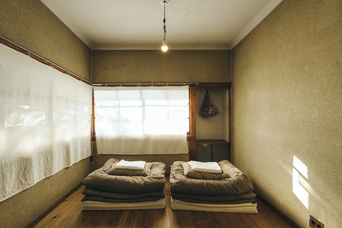 A room with two massage chairs, a large window with sheer curtains, and a hanging plant.