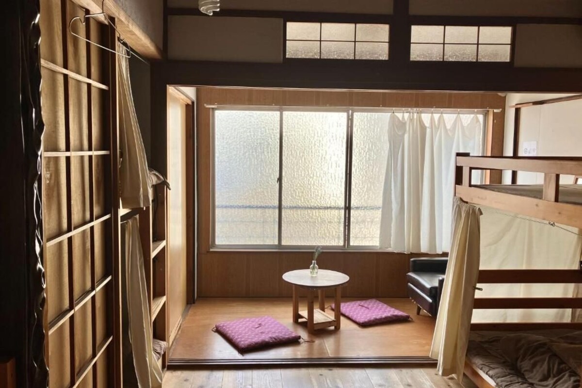 A room with a wooden floor, a small round table, a sofa, and a window with curtains.