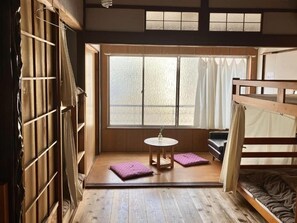 A room with a wooden floor, a small round table, a sofa, and a window with curtains. - Torii-Kuguru Hostel (Okayama)