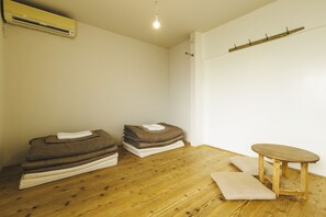 A room with a wooden floor, a small wooden table, and a stack of folded blankets. - Torii-Kuguru Hostel (Okayama)