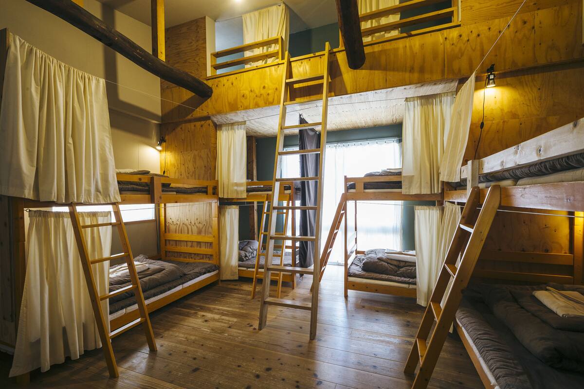 A dormitory-style room with bunk beds, wooden beams, and a ladder.