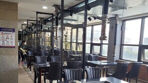Ein Restaurant mit schwarzen Ledersesseln und Tischen, großen Fenstern und einer Lüftungsanlage.