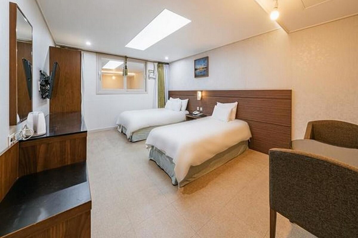 Une chambre d’hôtel avec deux lits, un bureau, une chaise et un grand miroir.