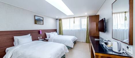 A hotel room with two beds, a desk, a TV, and a large window with curtains.