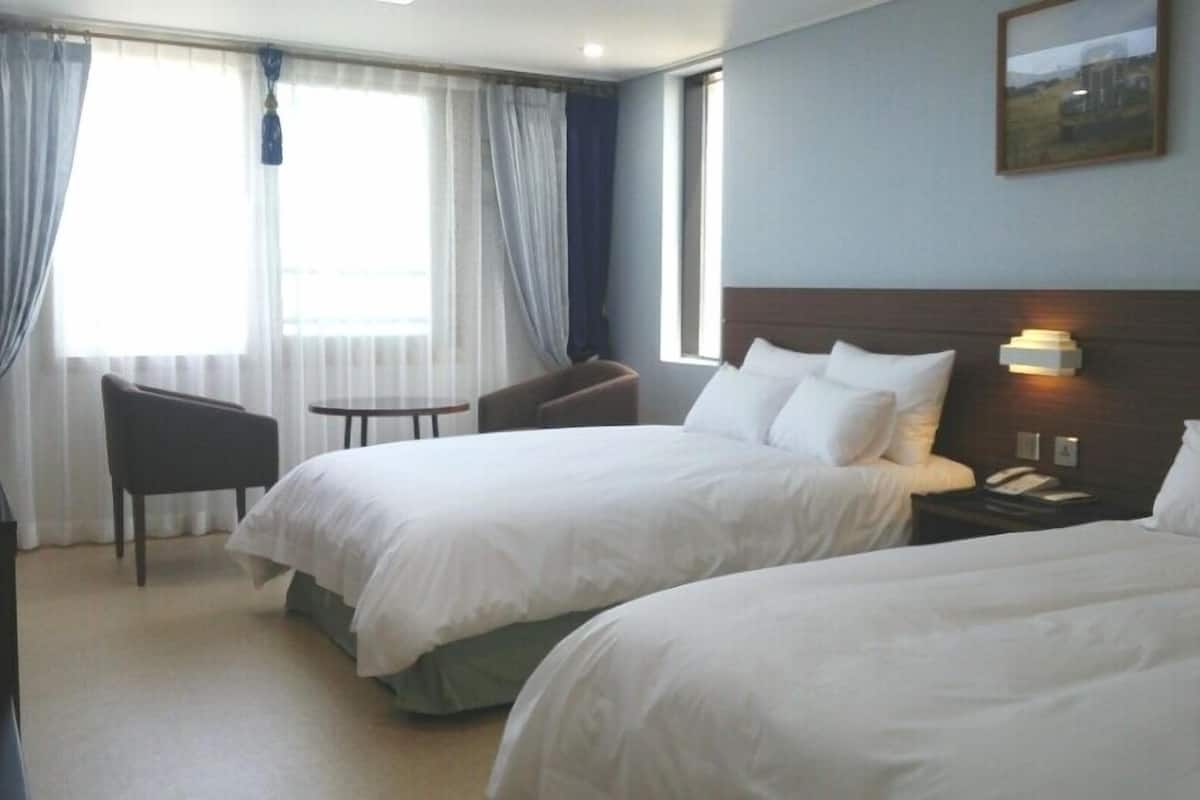 Een hotelkamer met twee bedden, een bureau, een stoel en een raam met gordijnen.
