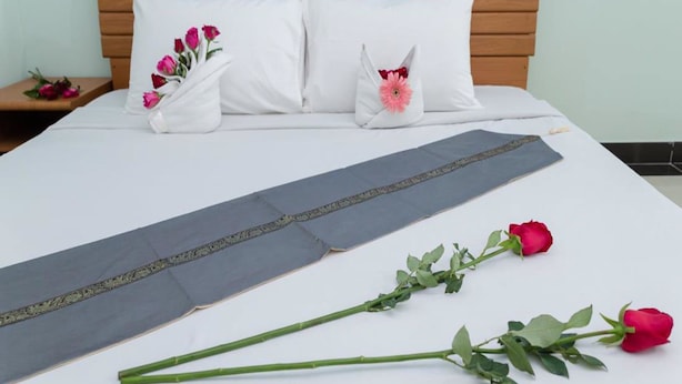 A neatly made bed with white pillows, a decorative pillow with a pink flower, and a bed runner. - The Garden Place (Nonthaburi)