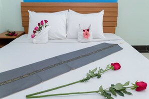 Una cama bien hecha con almohadas blancas, una almohada decorativa con una flor rosa y un corredor para la cama.