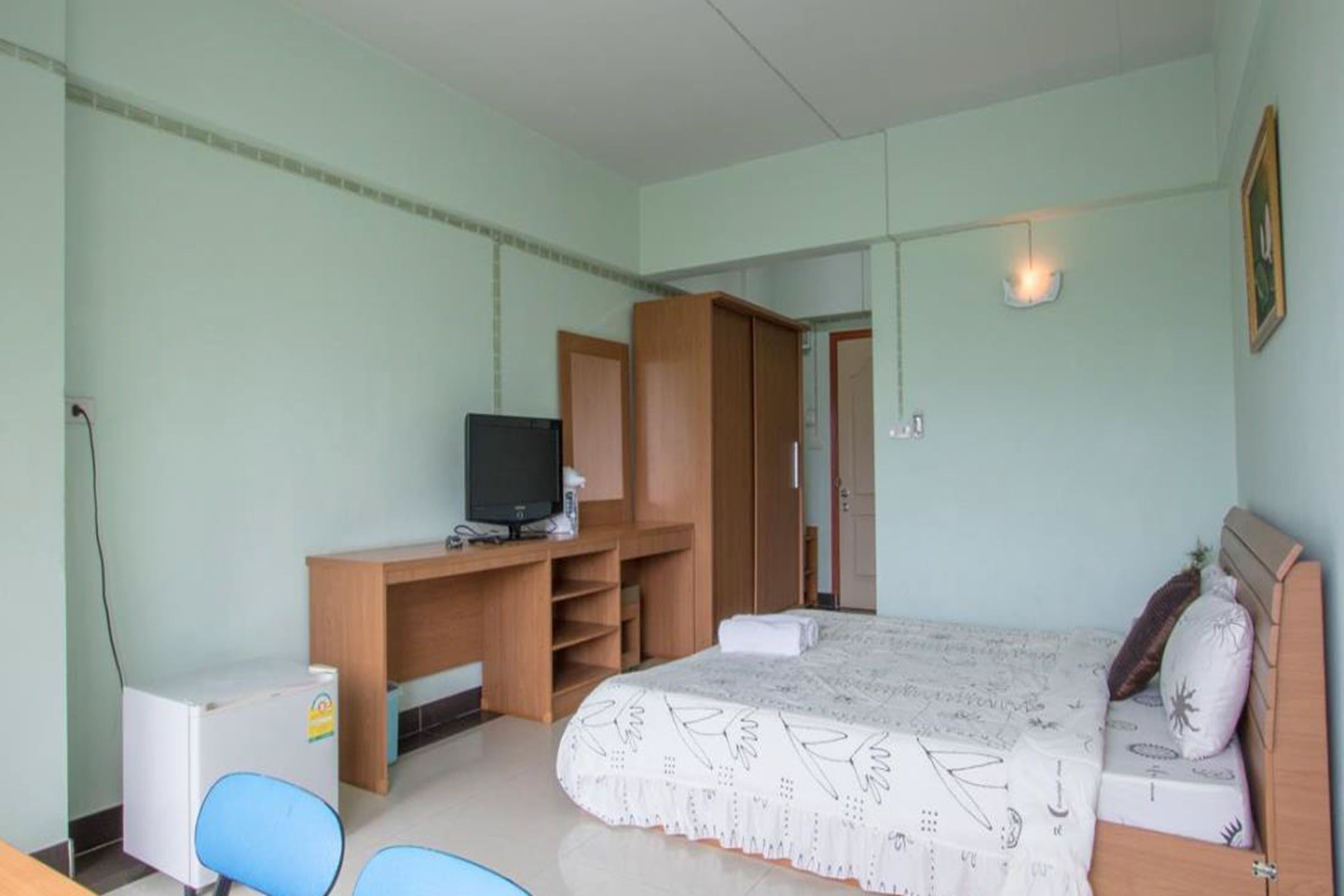 A bedroom with a bed, a desk with a television, a wardrobe, and a chair.