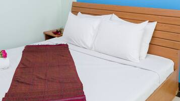 Cama com roupa de cama branca e um cobertor vermelho, cabeceira de madeira e mesa de cabeceira com uma flor.