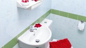 A bathroom with a white sink, green and white tiles, a red bath mat, and a toilet. - The Garden Place (Nonthaburi)