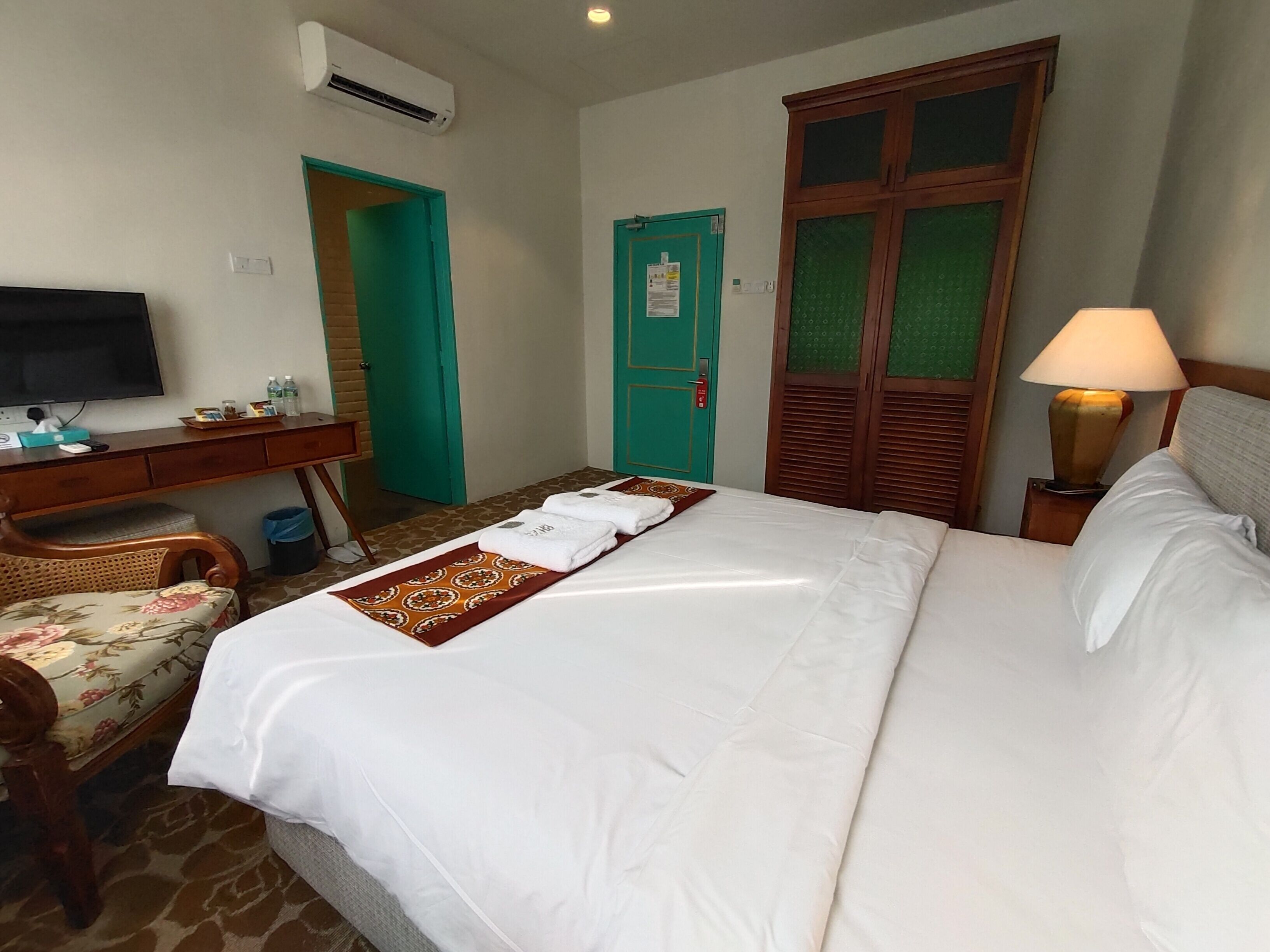 Quarto de hotel com cama, escrivaninha com computador, televisão e armário.