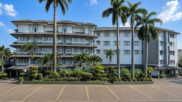 Un hotel de varios pisos con estilo arquitectónico tradicional, que cuenta con un estacionamiento y palmeras.