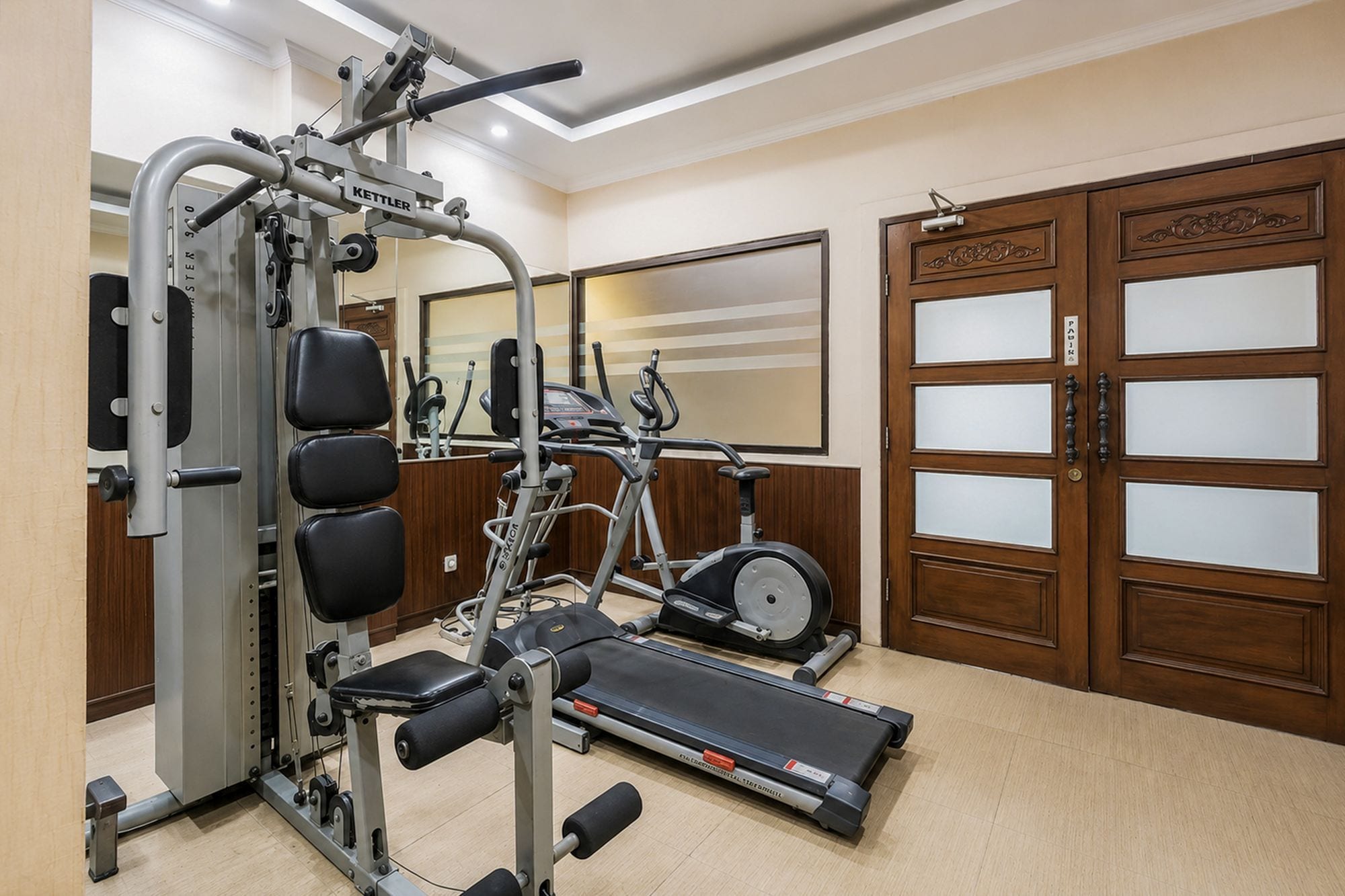 Un gimnasio con una máquina de pesas, una cinta de correr y un espejo.