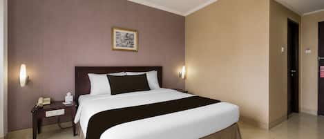 Une chambre d’hôtel avec un grand lit, des tables de chevet, un téléphone et un tableau encadré au mur.