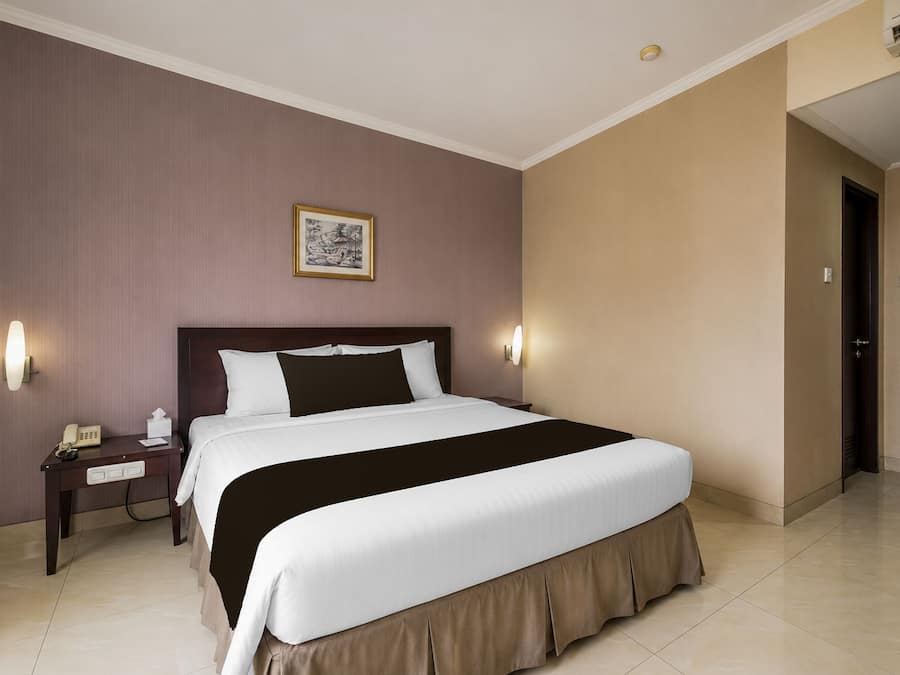 A hotel room with a large bed, bedside tables, a telephone, and a framed picture on the wall.