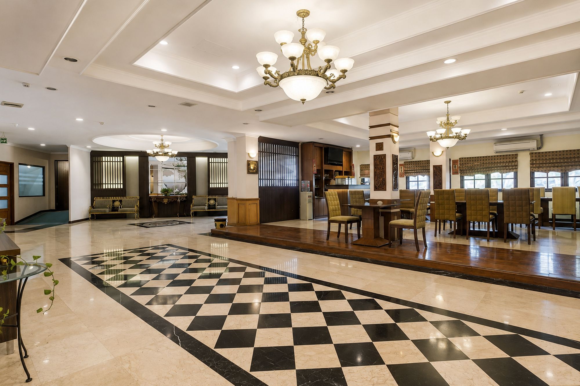 Eine Hotelhalle mit Schachbrettmuster-Boden, Sitzbereichen und Kronleuchtern.