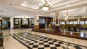 Eine Hotelhalle mit Schachbrettmuster-Boden, Sitzbereichen und Kronleuchtern.