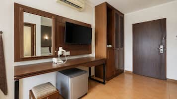 A hotel room with a wooden desk, a flat-screen TV, a mini-fridge, a telephone, and a door with a handle.