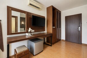 Quarto de hotel com escrivaninha de madeira, televisão de tela plana, mini-geladeira, telefone e porta com puxador.