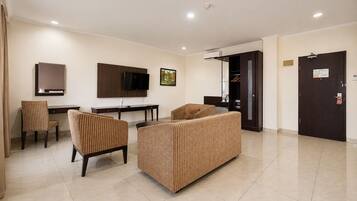 A hotel room with a flat-screen TV, a desk, two chairs, a sofa, and a door with a security lock.