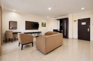 Habitación de hotel con televisor de pantalla plana, escritorio, dos sillas, sofá y puerta con cerradura de seguridad.