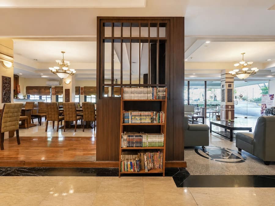 A hotel lobby with a reception desk, seating area, and a bookshelf filled with books.