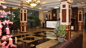 Um saguão de hotel com balcão de recepção, área de estar e plantas decorativas.