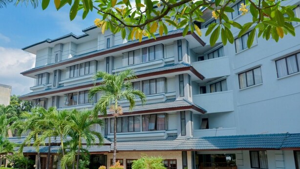 Hotel de vários andares com estilo arquitetônico tradicional, com varandas e estacionamento com palmeiras.