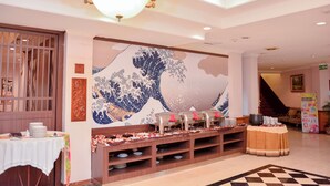 Um saguão de hotel com um mural tradicional japonês, um buffet montado e um candelabro.