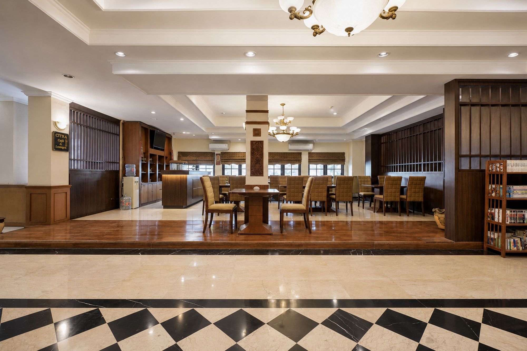 A spacious lobby with a checkered floor, a central seating area with tables and chairs, and a reception desk.