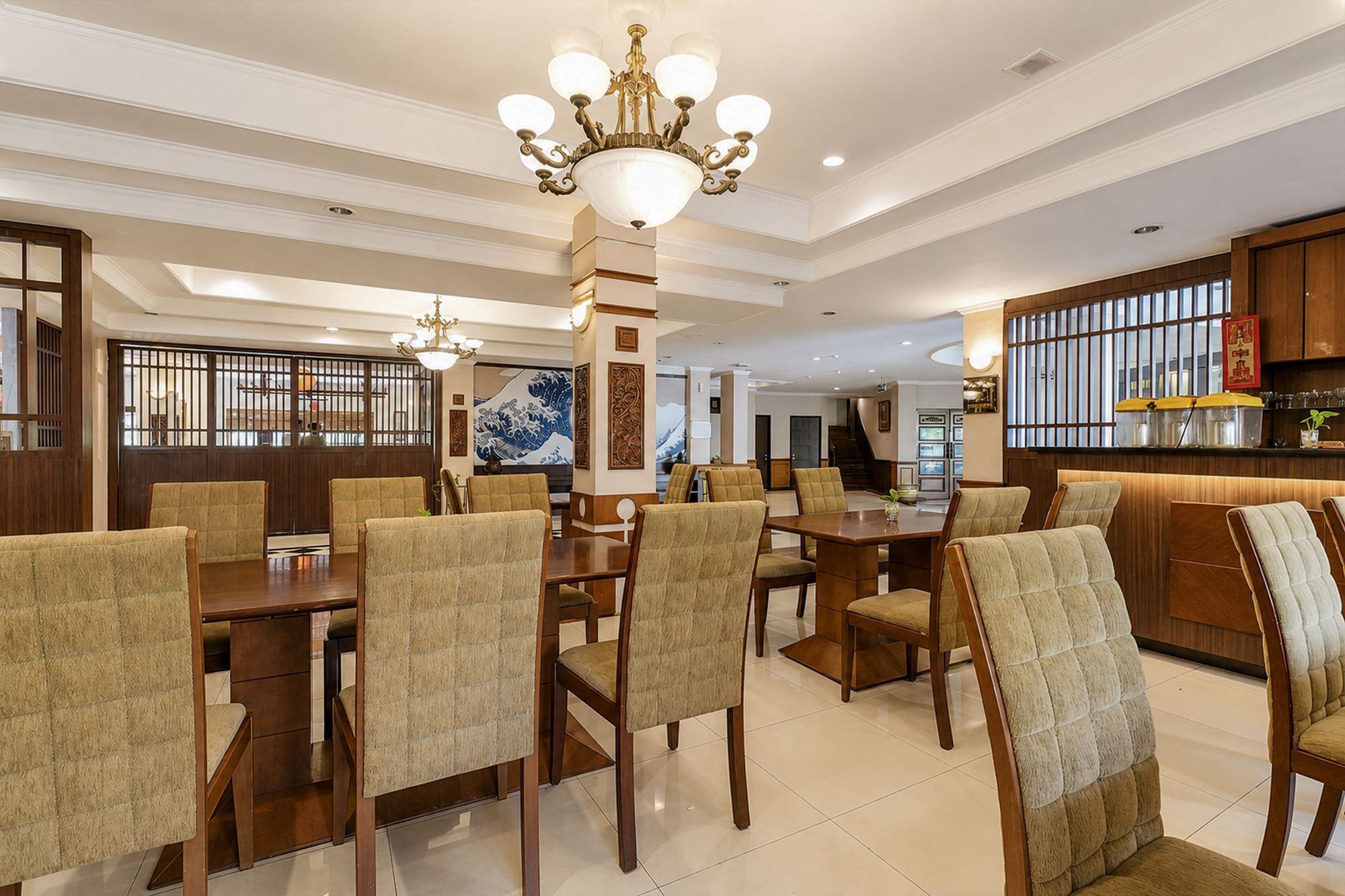 A spacious dining area with a high ceiling and a chandelier, featuring wooden furniture and a traditional Japanese artwork on the wall.