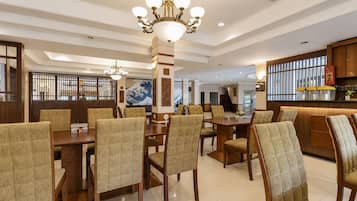 A spacious dining area with a high ceiling and a chandelier, featuring wooden furniture and a traditional Japanese artwork on the wall.