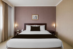 A hotel room with a large bed, two bedside tables, a nightstand, a framed picture on the wall, and a window with curtains. - Palette Citra Inn (Cikarang)