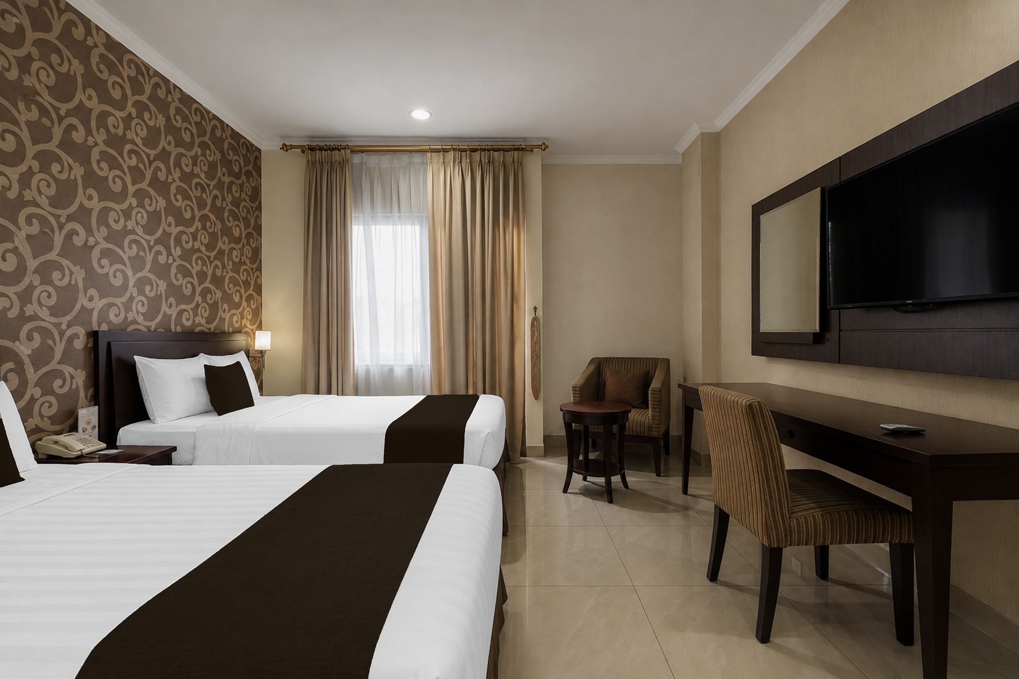 A hotel room with two beds, a desk, a chair, a television, and a window with curtains.