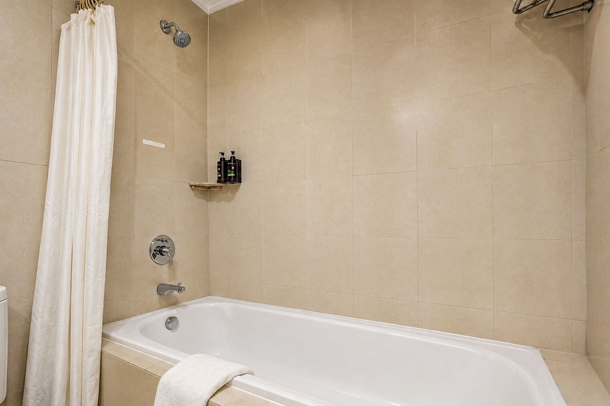 Un baño con bañera, cortina de ducha y un estante con artículos de aseo.