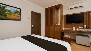 Ein Hotelzimmer mit einem Bett, einem Schreibtisch mit Flachbildfernseher, einem Kleiderschrank und einer Klimaanlage.