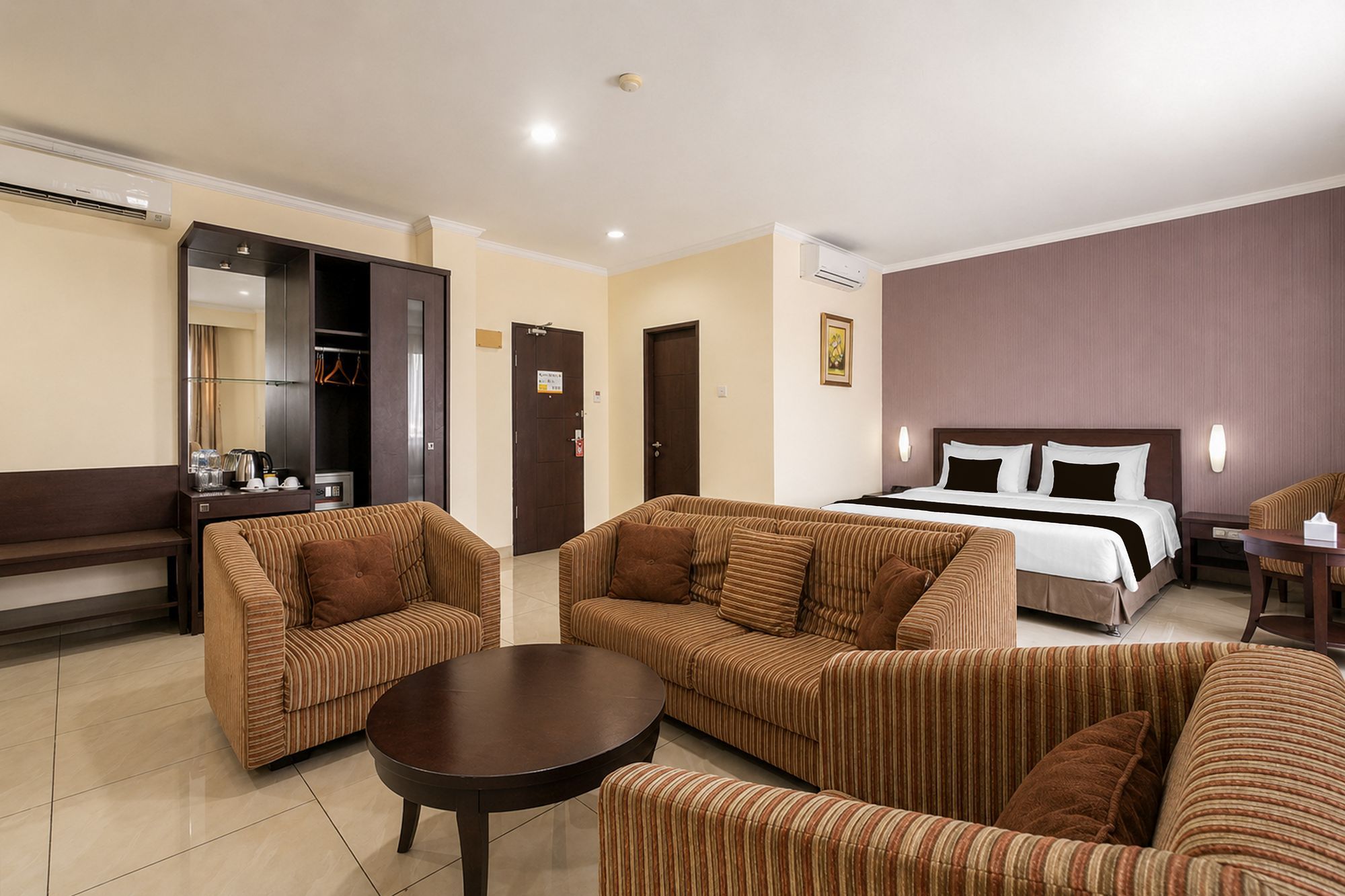 Ein Hotelzimmer mit einem Bett, zwei Sofas, einem kleinen Tisch, einem Spiegel und einem Kleiderschrank.